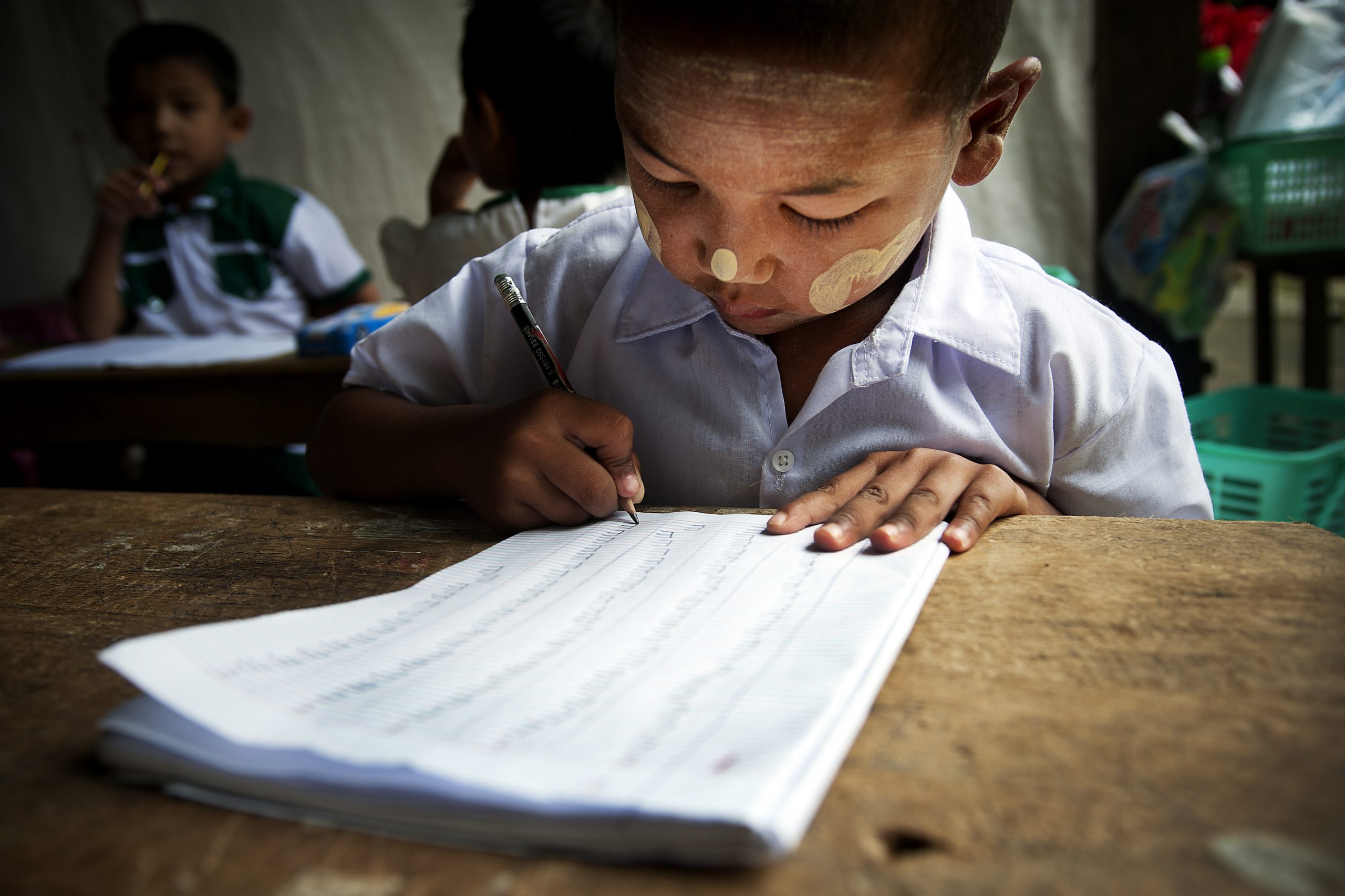 myanmarilaispoika kirjoittaa pulpetin äärellä paperille