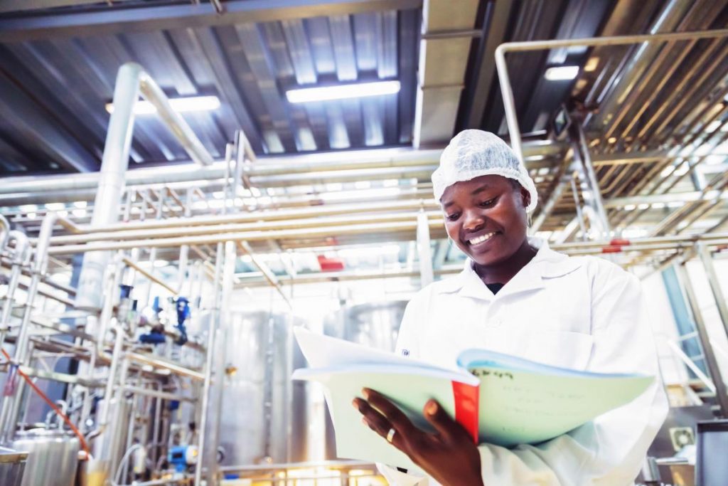 Female Factory Engineer Taking Notes While Standing Near the Heavy Machinery